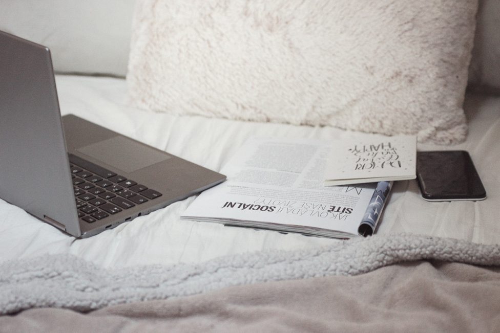 Web a Notebook na posteli s polštářem, telefonem a magazínem